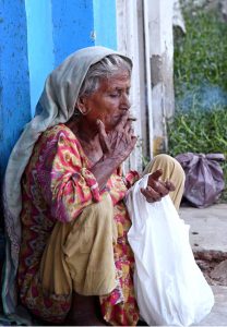 An elderly woman busy is smoking a cigarette near Jinnah Bagh Chowk