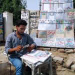 A man prepares engraved name slabs for graves outside a graveyard