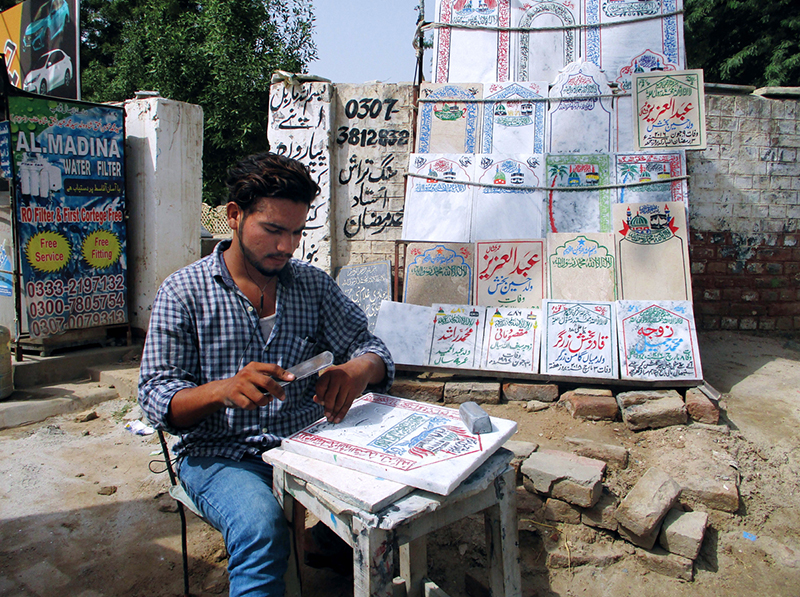 A man prepares engraved name slabs for graves outside a graveyard