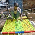 A worker prepares a traditional bed (Charpai) at his workplace on Risala Road