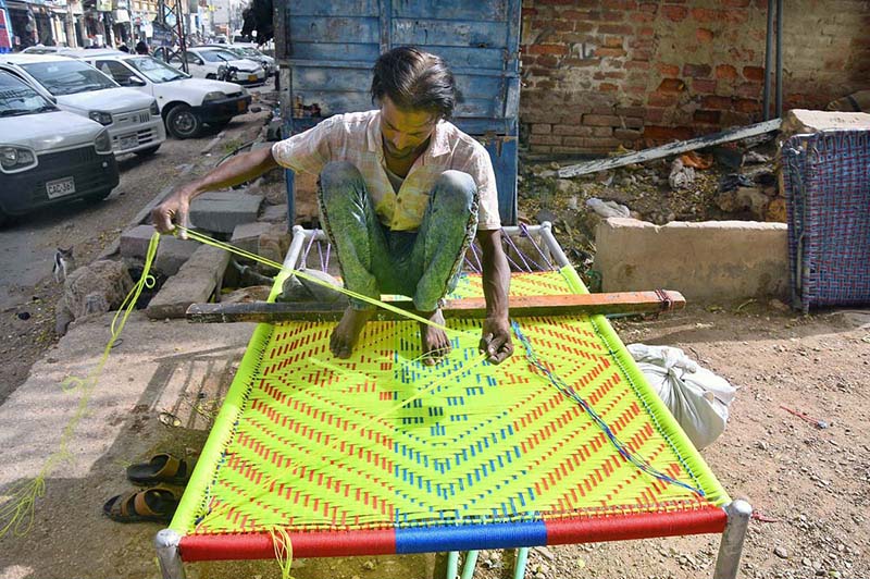 A worker prepares a traditional bed (Charpai) at his workplace on Risala Road