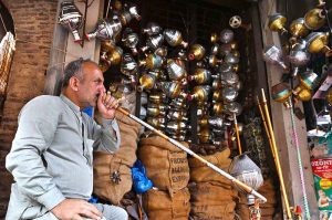 A shopkeeper smokes a hookah while displaying traditional hookah components (chilam) at his shop in the provincial capital