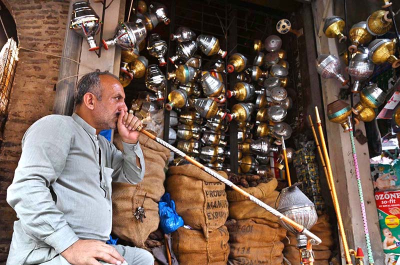 A shopkeeper smokes a hookah while displaying traditional hookah components (chilam) at his shop in the provincial capital