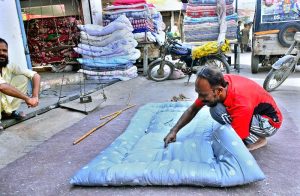 A worker hand-stitches a quilt for customers at his workplace as demand rises ahead of the winter season.