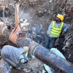 Workers weld a large gas pipeline in a deep trench as a crane holds the pipe in position during repair work in the Federal Capital