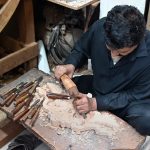 A craftsman carves a decorative design into a piece of wood at his workshop in the Pindora area