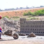A lady labourer pushing hand cart loaded with mud for preparing bricks at brick kiln, Tando Hyder
