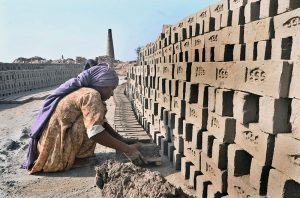 A lady labourer pushing hand cart loaded with mud for preparing bricks at brick kiln, Tando Hyder