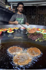 A vendor lifts a freshly fried chapli kebab from sizzling oil to attract customers at his shop in Banni Chowk.