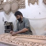 A skilled man carving wood of a furniture piece at his workplace