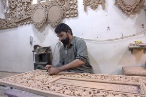 A skilled man carving wood of a furniture piece at his workplace