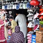A woman is selecting and purchasing shoes from a stall in Sunday Bazaar at Peshawar Mor in the Federal Capital