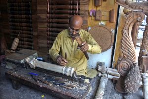 A skilled man carving wood of a furniture piece at his workplace