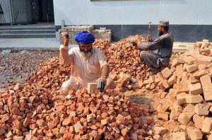 Labourers break bricks into smaller pieces using hammers at a construction site, earning their livelihood through manual labour.