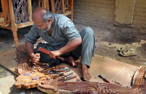 A craftsman uses traditional hand tools to carve intricate designs into a wooden structure at his workshop, showcasing the skill and precision of traditional woodworking.