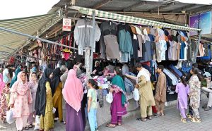 A woman is selecting and purchasing shoes from a stall in Sunday Bazaar at Peshawar Mor in the Federal Capital