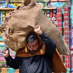 A labourer on the way while carrying heavy vegetable sack after unloading from transport at vegetable market