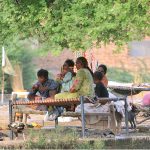 A nomadic family resting on woven cots beneath a tree along a canal bank on the city's outskirts
