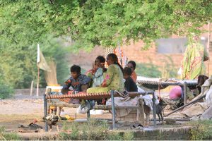 A nomadic family resting on woven cots beneath a tree along a canal bank on the city's outskirts