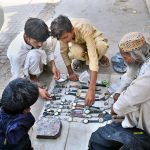 Customers browse wristwatches displayed by a roadside vendor on the footpath at Station Road