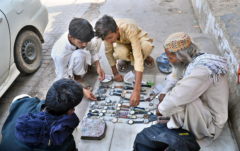 Customers browse wristwatches displayed by a roadside vendor on the footpath at Station Road