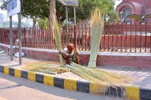 An elderly woman displays brooms for sale to earn a livelihood at Ghanta Ghar Chowk.