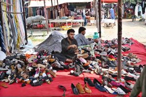 A woman is selecting and purchasing shoes from a stall in Sunday Bazaar at Peshawar Mor in the Federal Capital