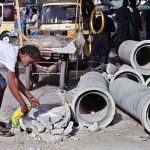 A drug addict removes iron from a discarded sewerage pipe lying on Mission Road in the old city area, highlighting the need for greater attention by the concerned authorities
