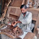 A furniture worker carves intricate designs on wood at his workplace