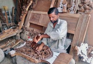 A furniture worker carves intricate designs on wood at his workplace