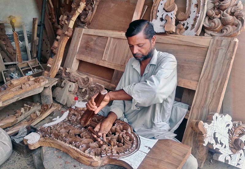 A furniture worker carves intricate designs on wood at his workplace