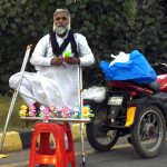 A disabled vendor displays children’s toys for sale while standing beside his tricycle along Ferozepur Road