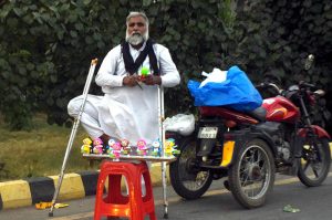 A disabled vendor displays children’s toys for sale while standing beside his tricycle along Ferozepur Road