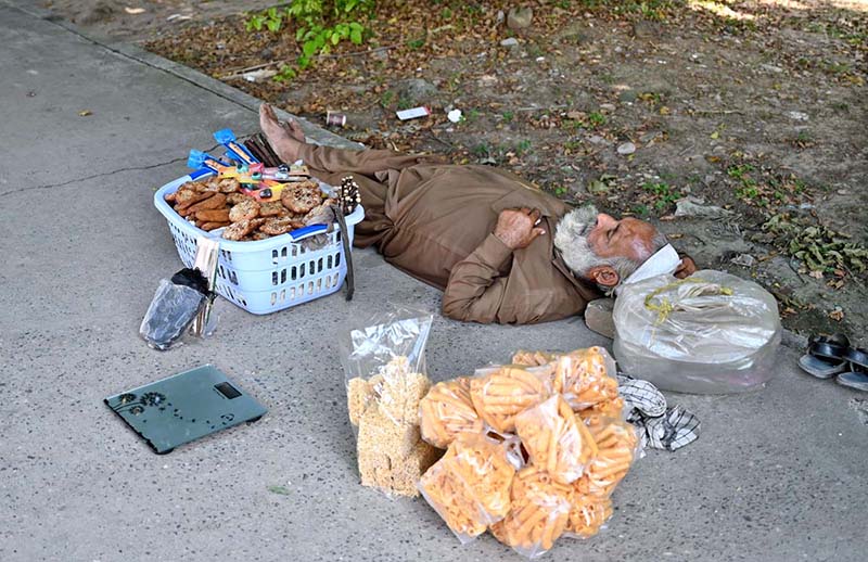 An elderly vendor taking a nap on the footpath in the shade of a tree in the Federal Capital