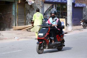 A woman rides an electric scooter through a busy city street.