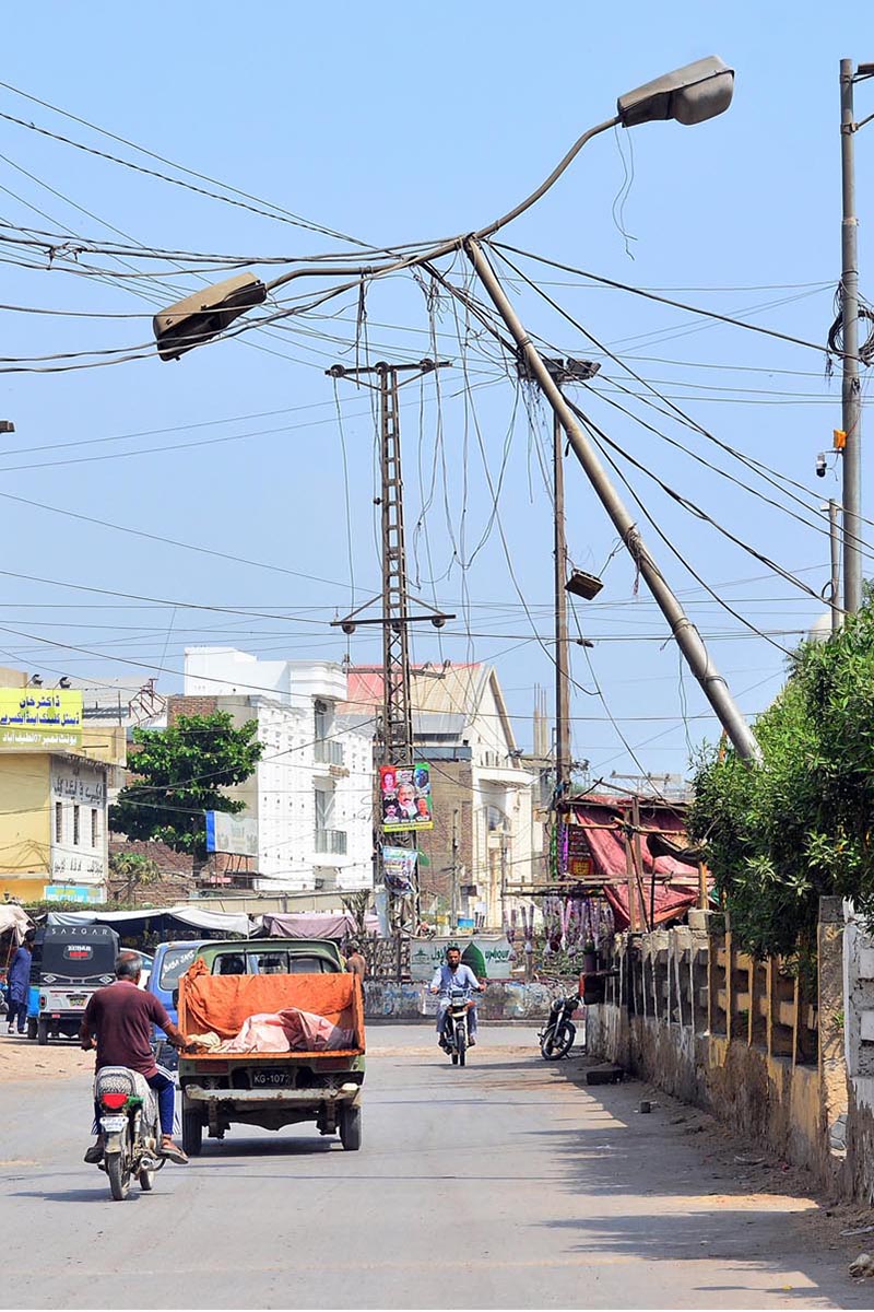 An electricity pole leans dangerously towards the road, posing a potential risk to commuters in Latifabad Unit No. 7