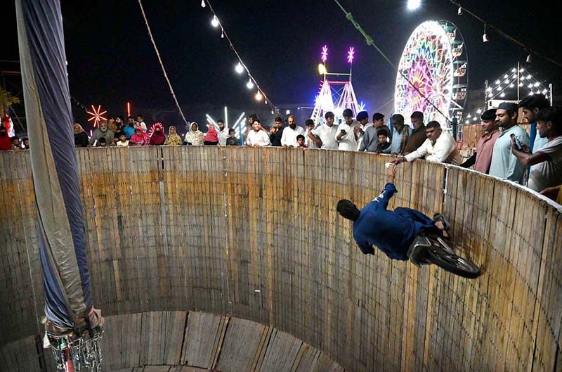 Stunt biker perform in the Well of Death as spectators watch during the Dada Hanjer Pir local Mela at a fairground near Multan Road