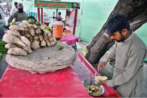 A street vendor prepares a plate of delicious coal-roasted sweet potatoes for a customer on roadside his setup.