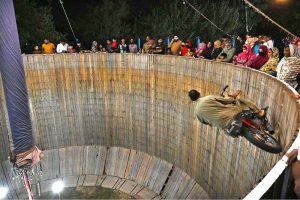 Stunt biker perform in the Well of Death as spectators watch during the Dada Hanjer Pir local Mela at a fairground near Multan Road