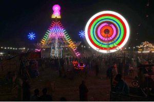 People watch and enjoying a Ferris wheel at night with colorful light during a Dada Hanjer Pir local mela festival at fair ground near Multan road