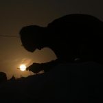 A labourer stitches a sack, silhouetted against a mesmerizing sunset in the Federal Capital