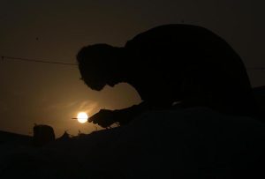 A labourer stitches a sack, silhouetted against a mesmerizing sunset in the Federal Capital