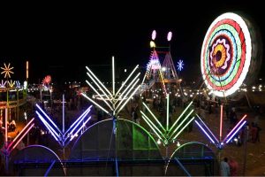 People watch and enjoying a Ferris wheel at night with colorful light during a Dada Hanjer Pir local mela festival at fair ground near Multan road