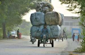 A tricycle rider is transporting an over loaded with recyclable waste packed in sacks along a busy road, raising road safety concerns.