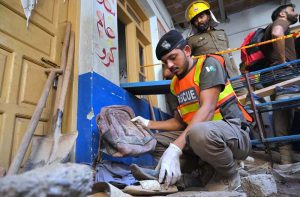 A Rescue 1122 official collects the belongings of schoolchildren from the rubble of a collapsed school building in Dir Colony, where several students were killed and injured.