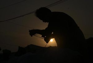 A labourer stitches a sack, silhouetted against a mesmerizing sunset in the Federal Capital