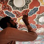 A skilled artisan meticulously paints intricate floral and geometric patterns on a ceiling, showcasing the rich tradition of decorative ceiling art that has been an integral part of Pakistan's architectural heritage for centuries