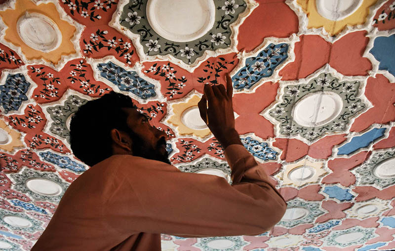 A skilled artisan meticulously paints intricate floral and geometric patterns on a ceiling, showcasing the rich tradition of decorative ceiling art that has been an integral part of Pakistan's architectural heritage for centuries
