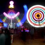 People watch and enjoying a Ferris wheel at night with colorful light during a Dada Hanjer Pir local mela festival at fair ground near Multan road