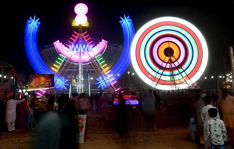 People watch and enjoying a Ferris wheel at night with colorful light during a Dada Hanjer Pir local mela festival at fair ground near Multan road